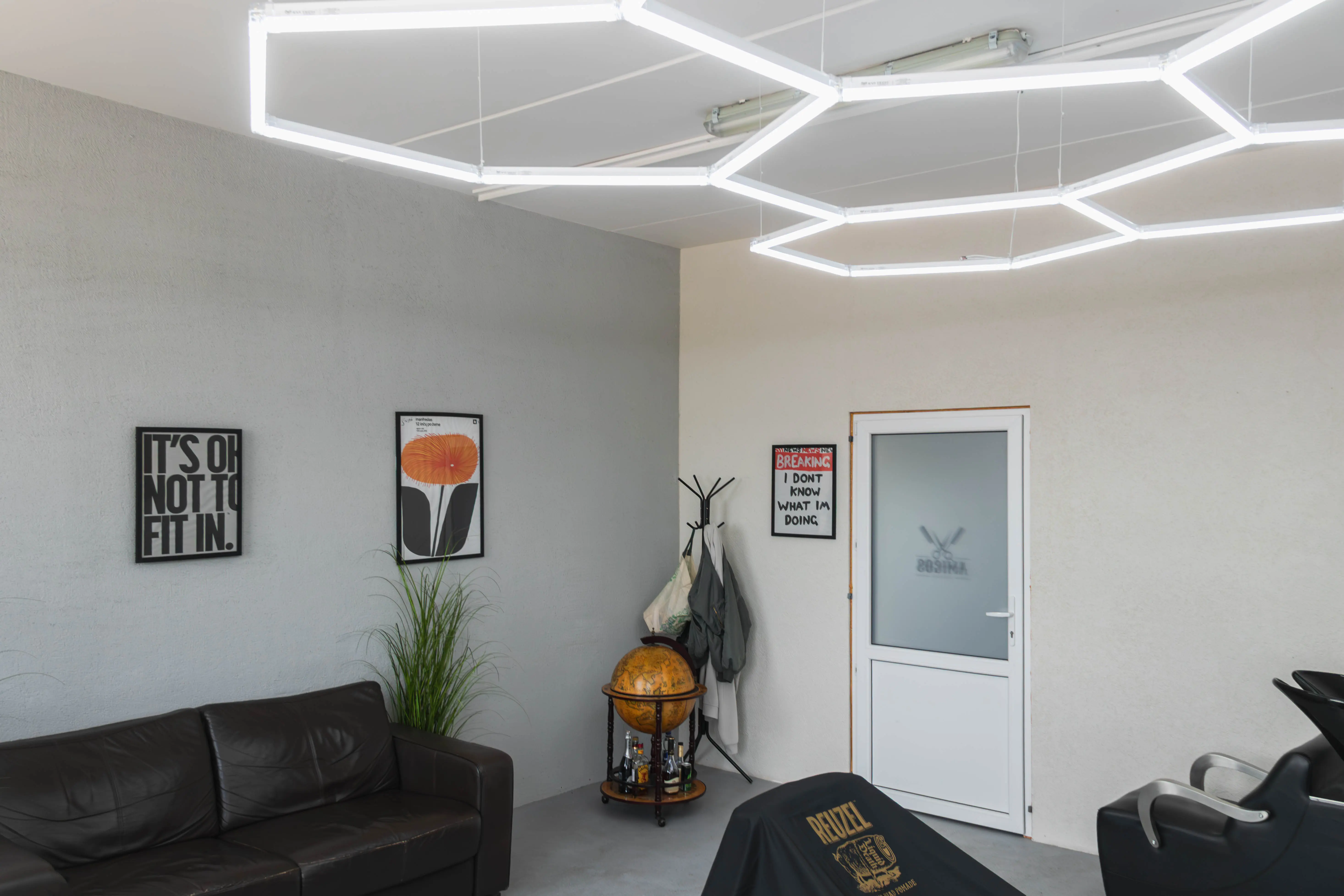 Amigos Barbershop laukimo zona - odinė sofa, gaublys-baras ir AMIGOS logotipas ant durų